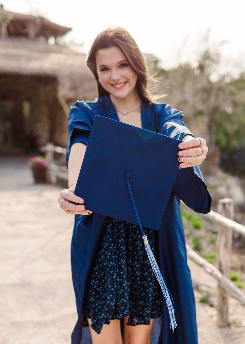 Graduate holding up a blue graduation cap near stone pillars.