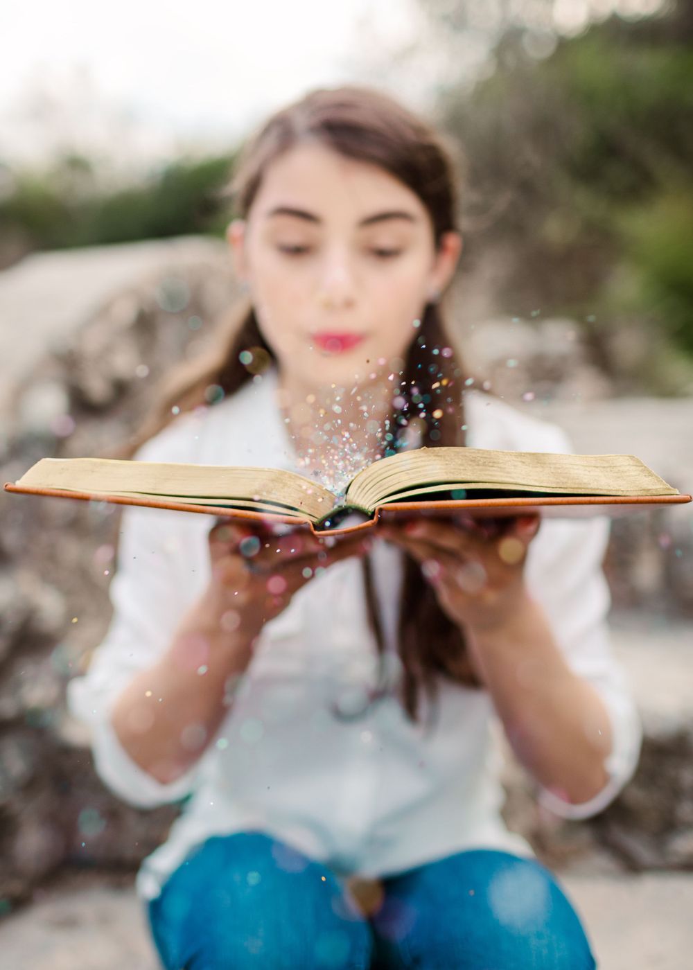 Person blowing glitter from open book in artistic graduation photo.
