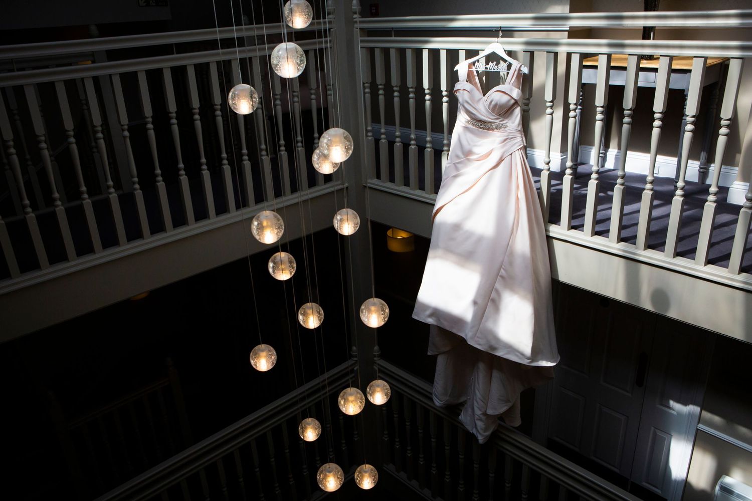 Elegant wedding dress hanging on balcony railing illuminated by warm glowing pendant lights below.
