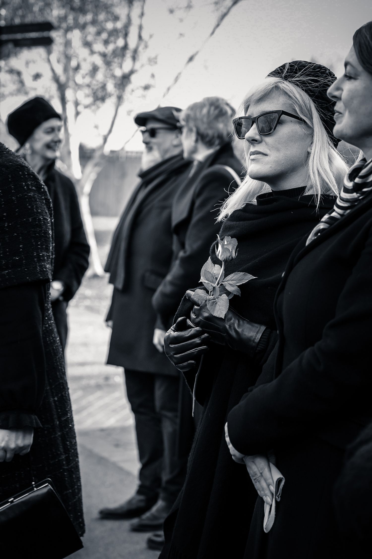 Group of people in dark coats gathered outdoors in black and white.