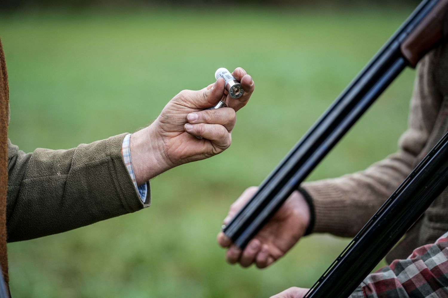 Close-up of hands loading shotgun shells during hunting activity.