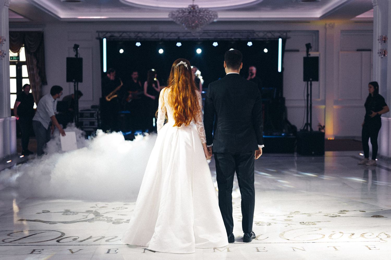 Newlyweds stand on foggy dance floor during their first dance at wedding reception.