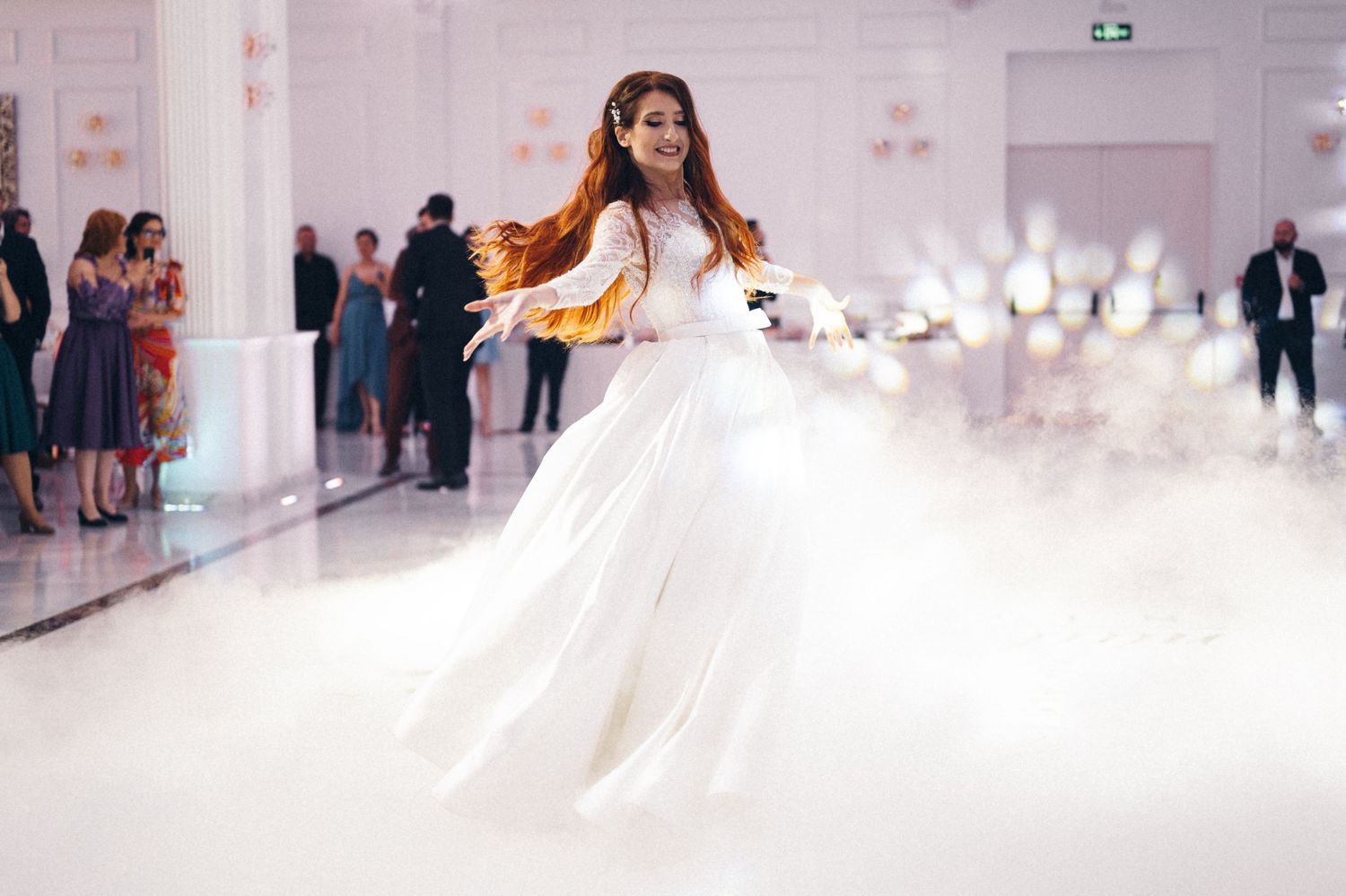 Bride in flowing white gown twirls on misty dance floor during wedding reception.
