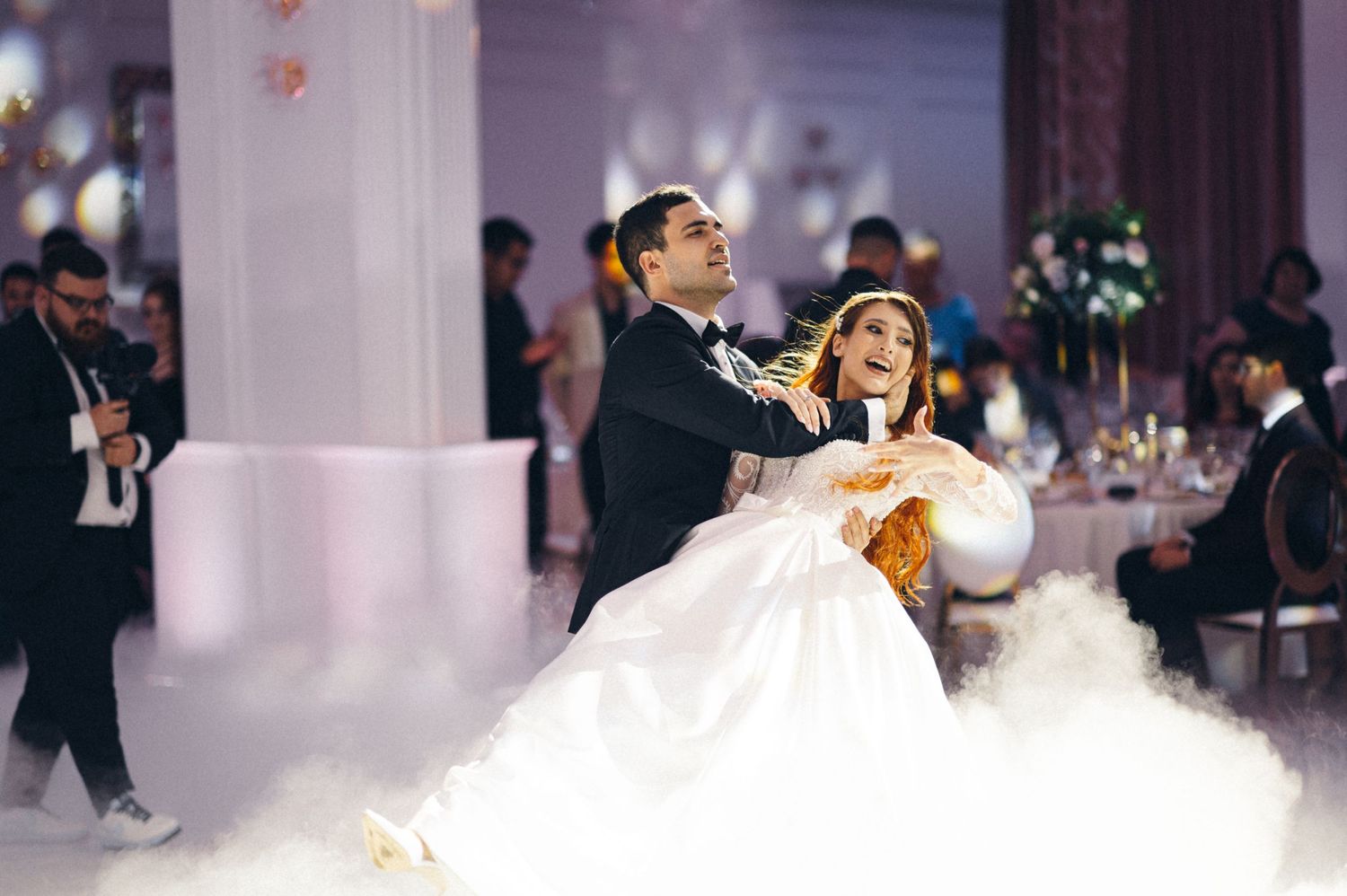 Couple performs energetic dance move during their wedding reception with fog effects.