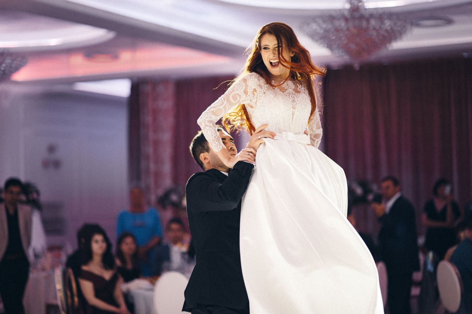 Dynamic shot of bride being lifted during wedding dance with dress flowing.