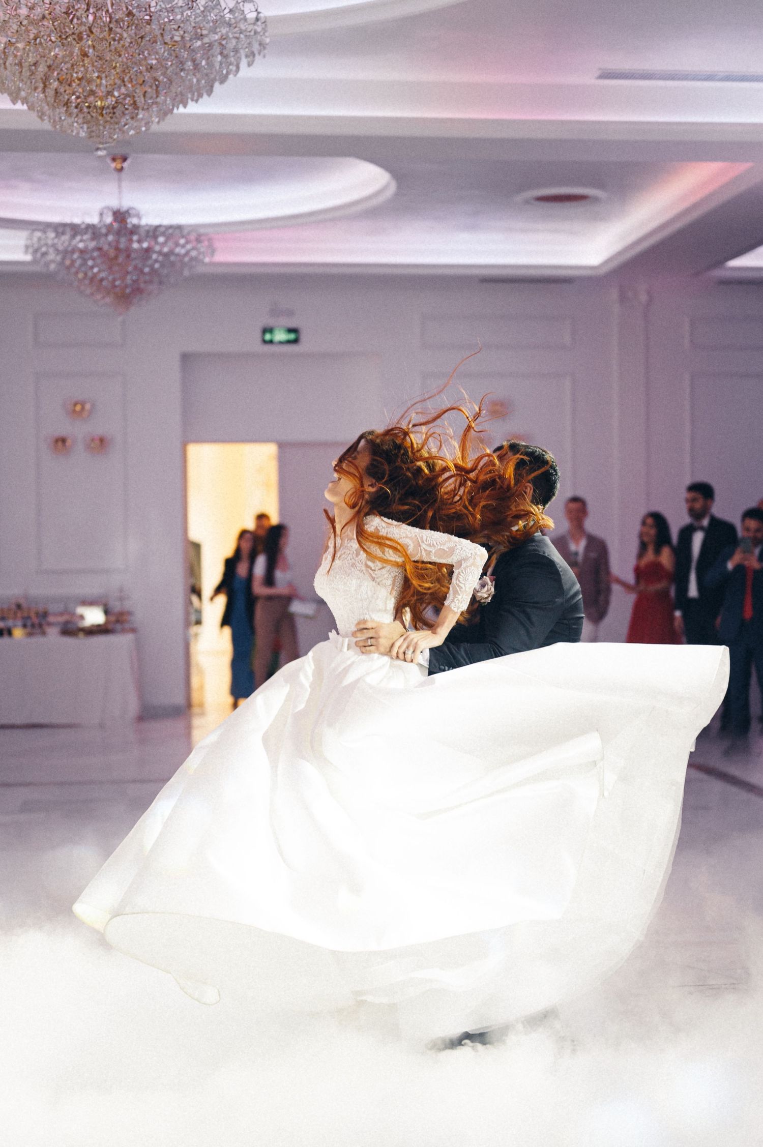 Couple performs romantic dance lift with fog effects at wedding reception.