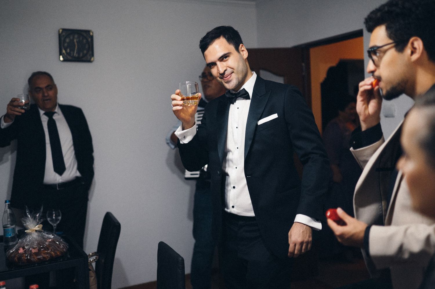 Wedding party members in formal attire sharing drinks and laughter.