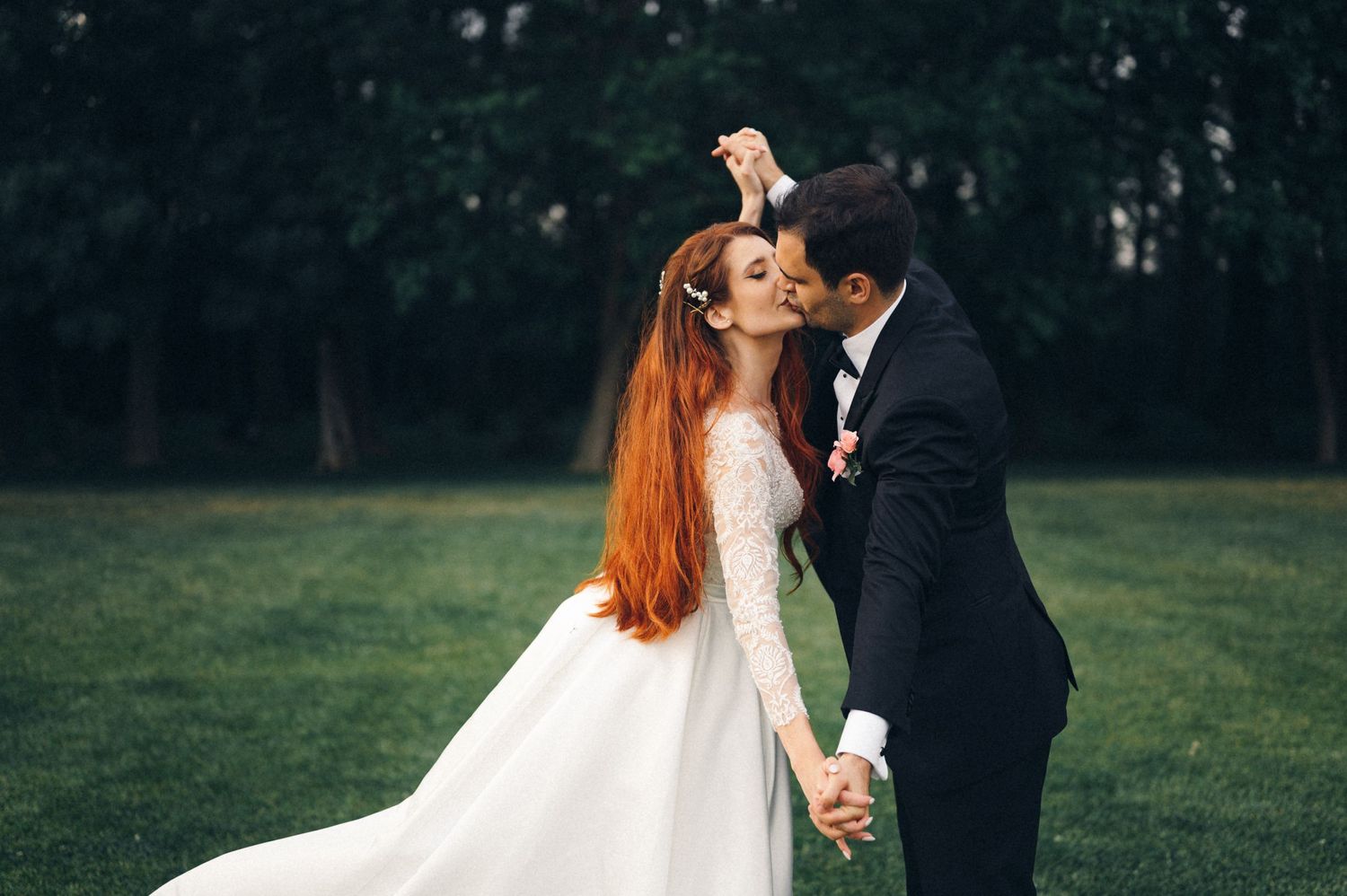A couple shares an intimate dance moment outdoors in formal wedding attire.