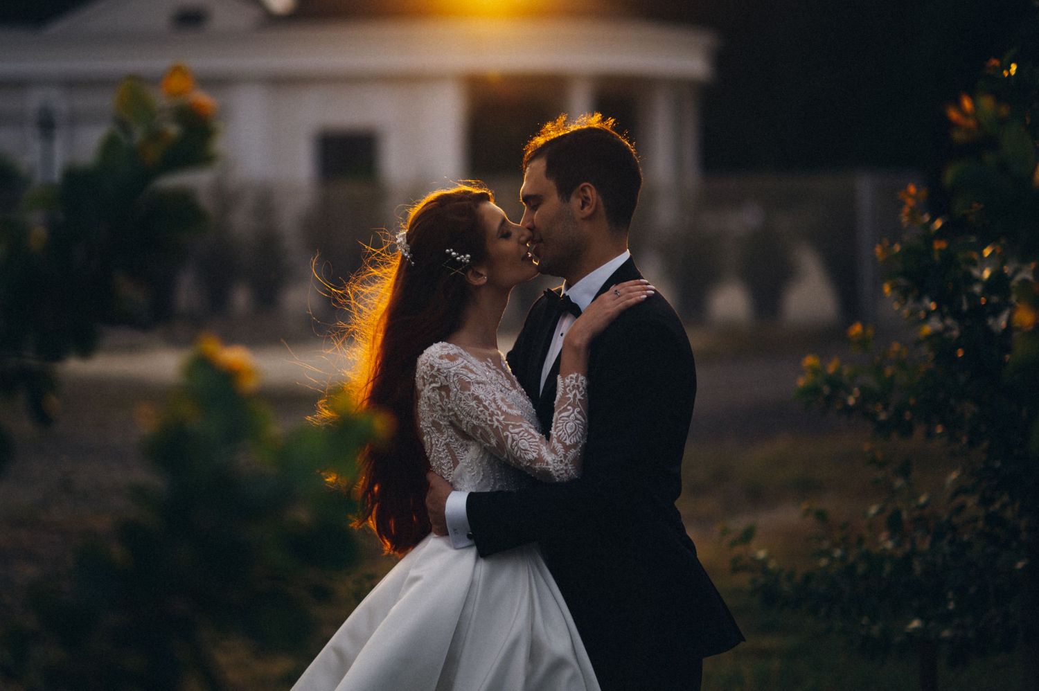 A romantic sunset wedding portrait in front of an elegant building with golden backlight.