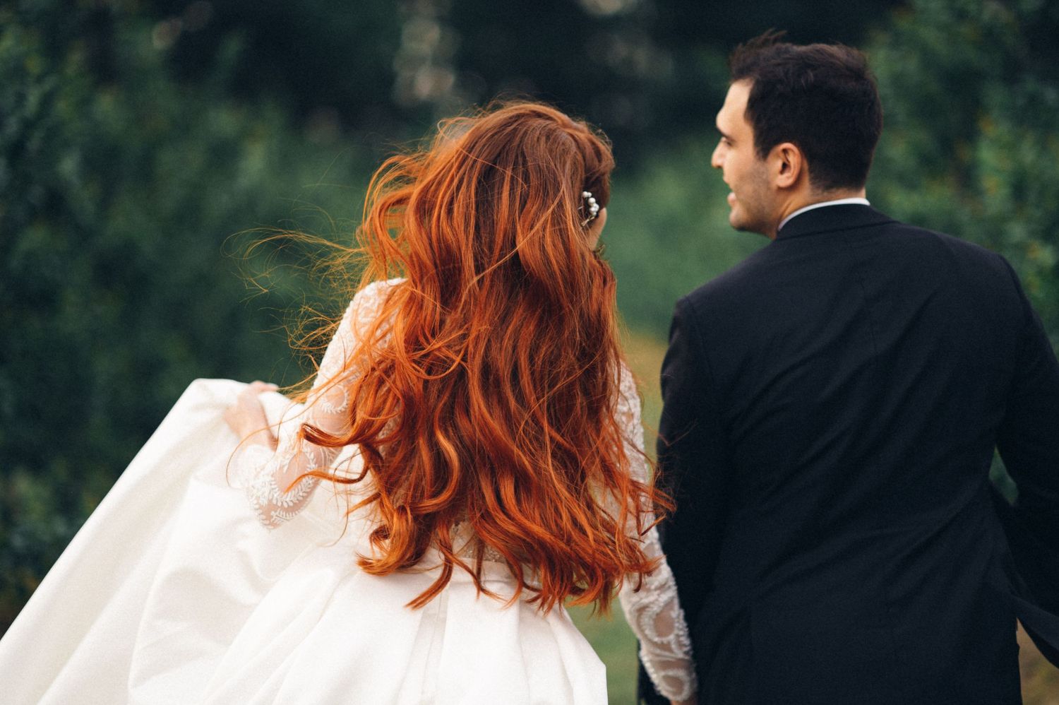 A wedding couple photographed from behind walking through a lush garden setting.