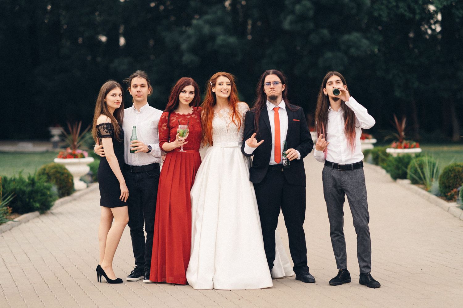 A wedding party poses together outdoors wearing formal attire in black, red and white.