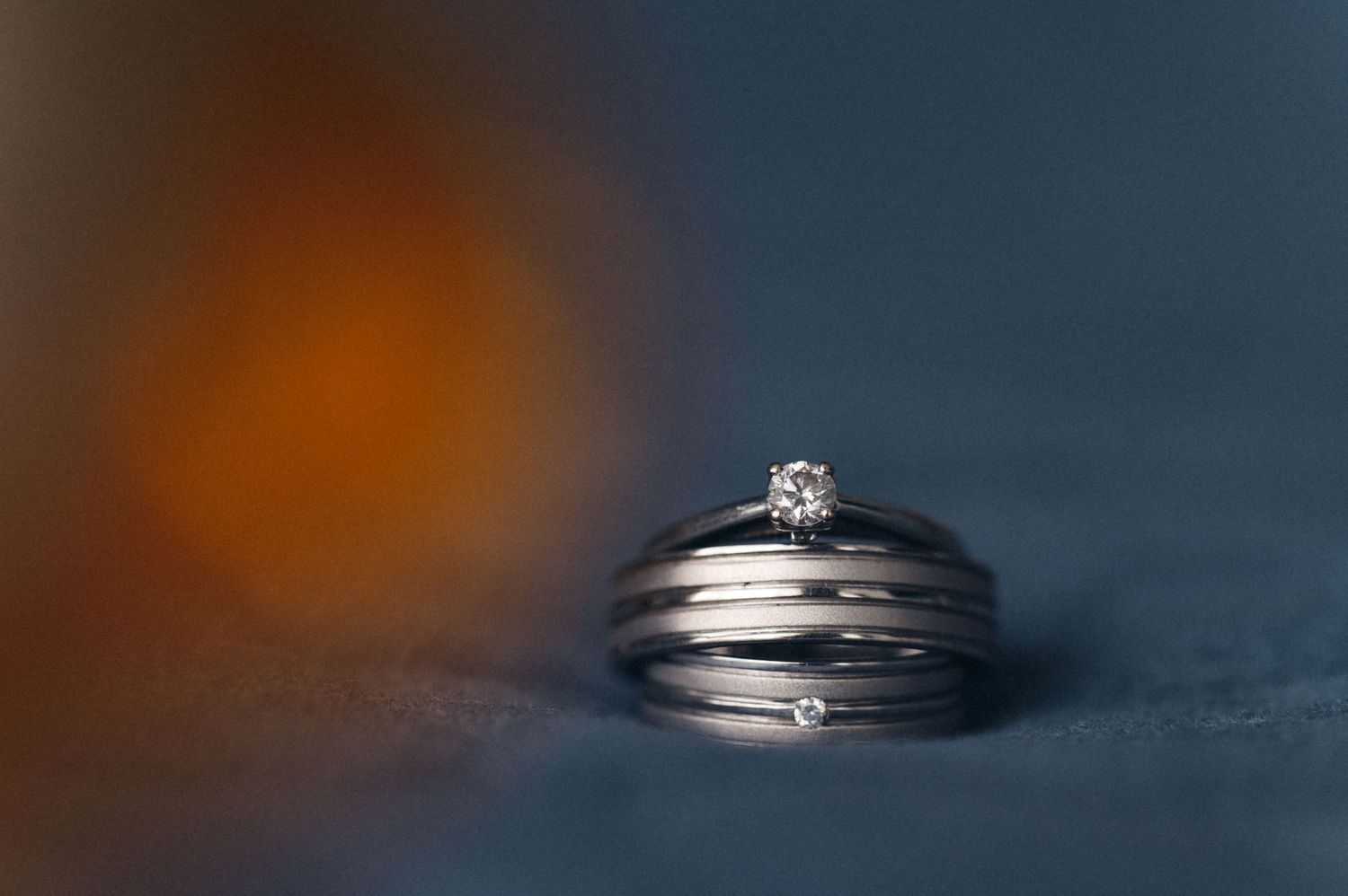 Wedding rings with diamond engagement ring on dark textured surface.
