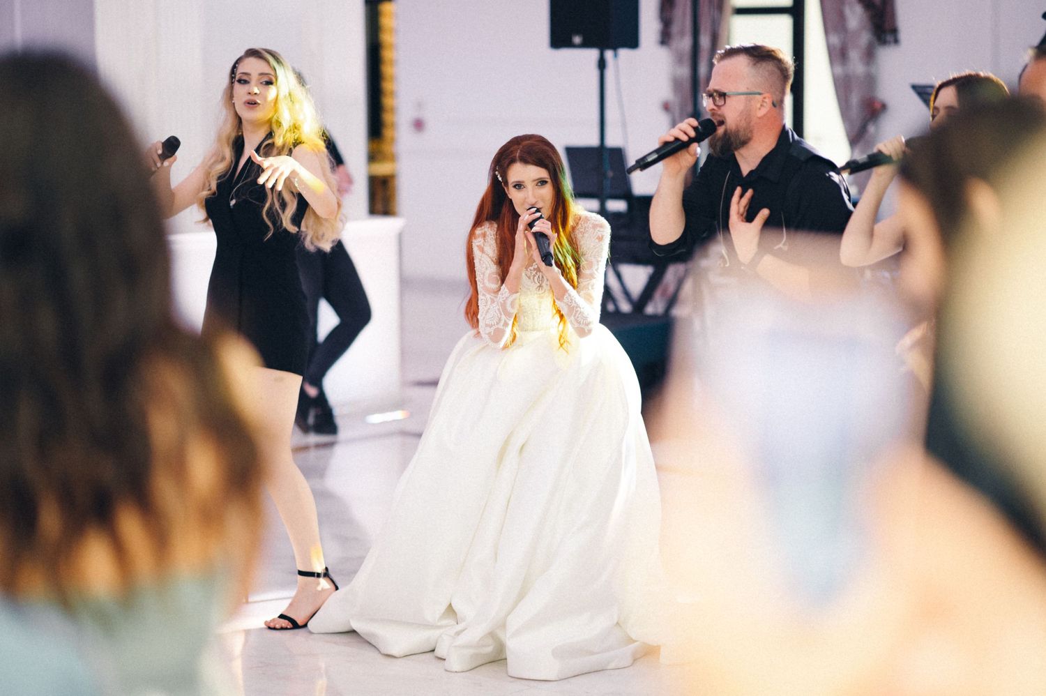 Wedding band performers entertain guests during a celebration in a bright indoor venue.