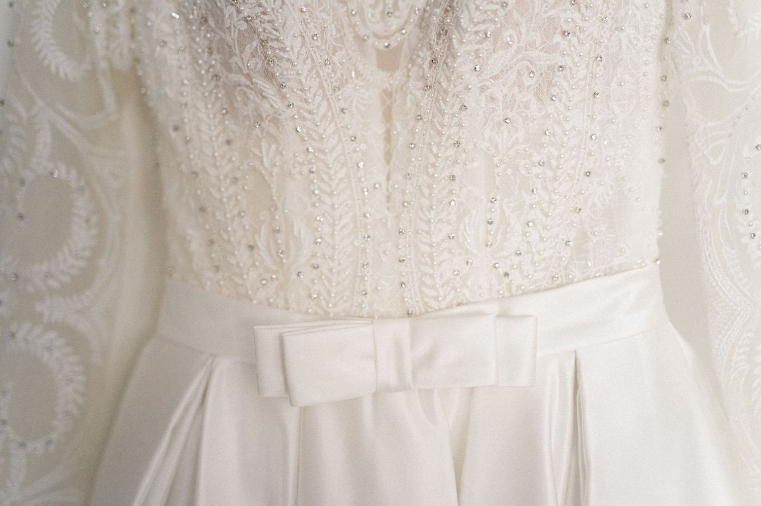 Close-up detail of a white lace wedding dress bodice with delicate floral patterns and pleated waist.