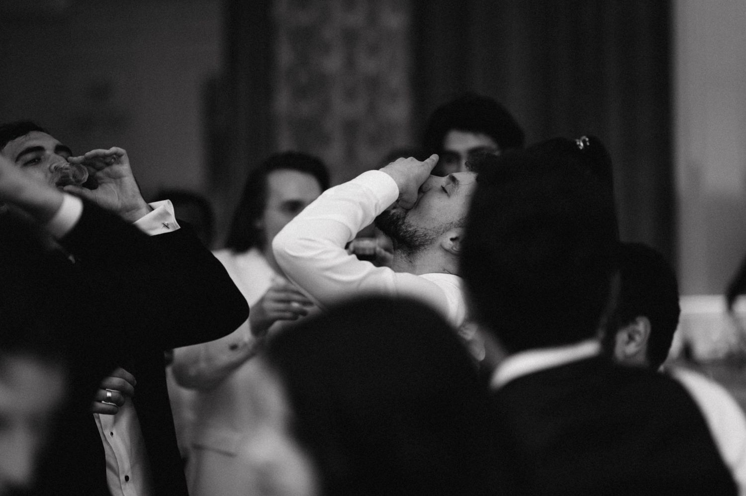 Black and white photo of guests taking shots at a lively wedding reception.