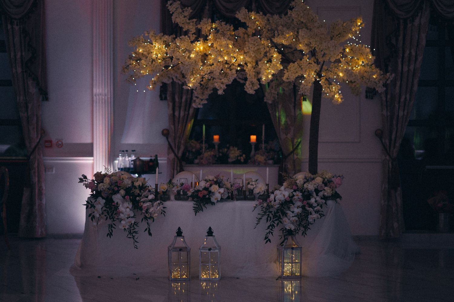Elegant wedding decor featuring illuminated golden branches and floral arrangements.
