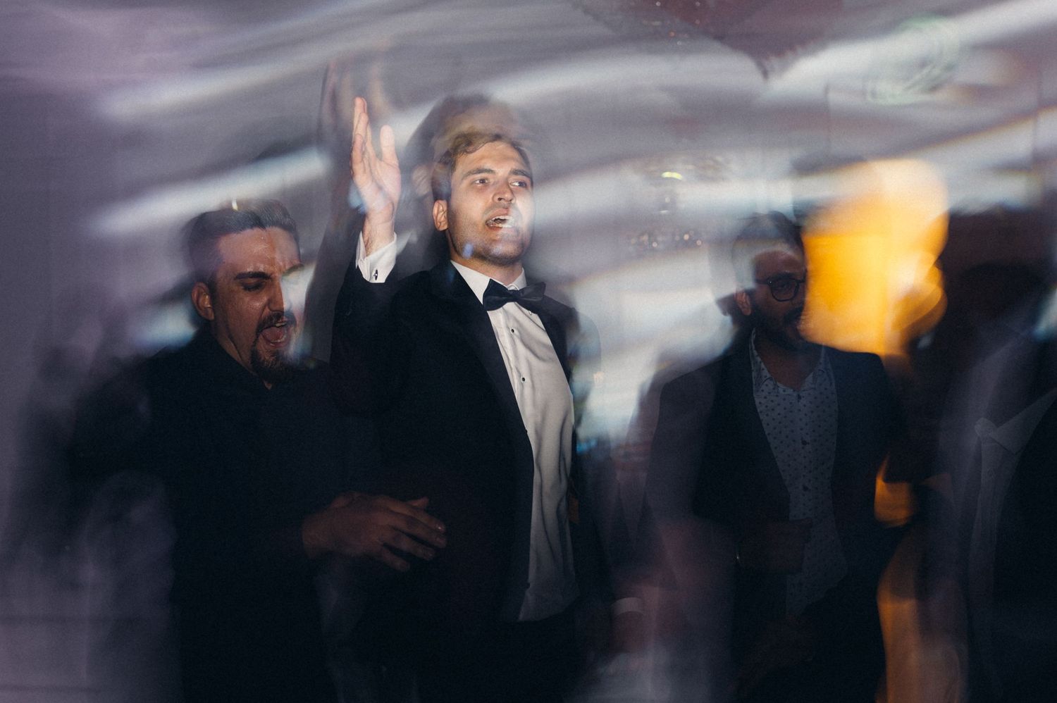 Wedding guest in formalwear gesturing enthusiastically during reception celebrations.