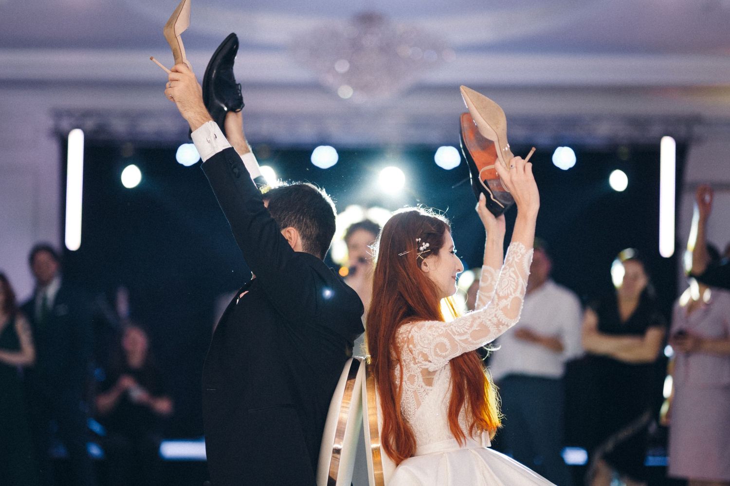 Wedding couple raises their shoes in the air during a festive dance tradition at their reception.