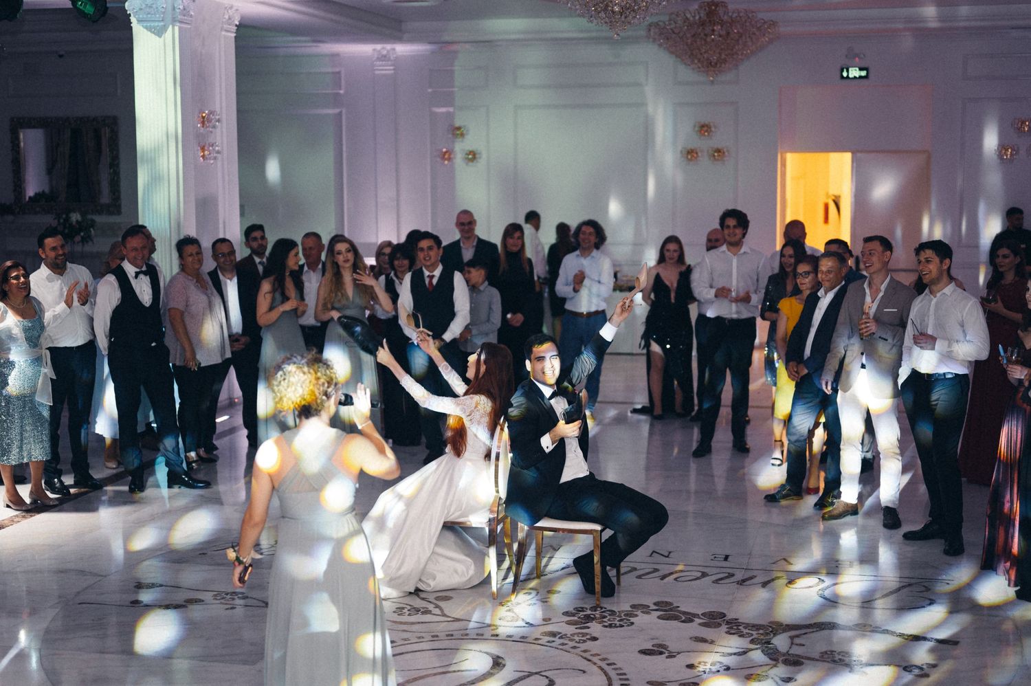 Wedding guests dance energetically on an illuminated white dance floor during the reception.