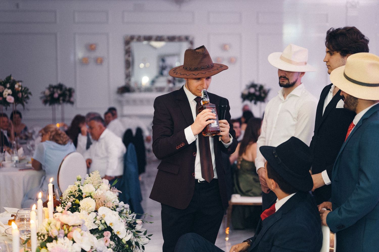 Wedding guests gather around a decorated table with white floral centerpieces during dinner service.