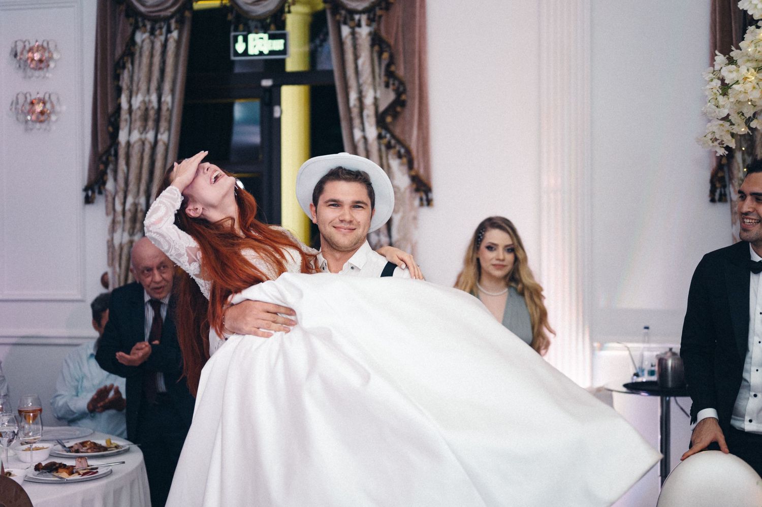 A celebratory wedding moment with traditional carrying pose during indoor reception.