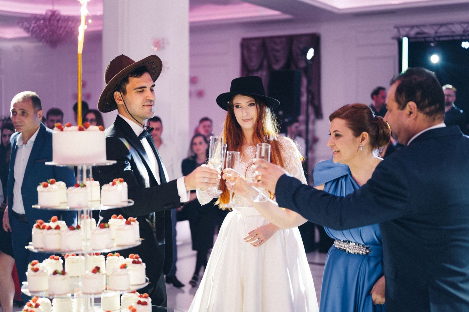 Wedding celebration around a multi-tiered cake display at an elegant indoor reception.
