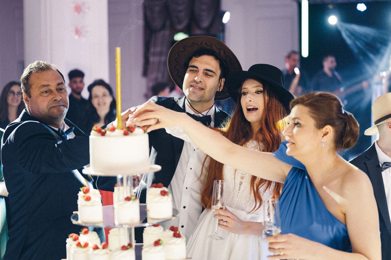 Wedding party gathers around an elegant tiered cake during the reception celebration.
