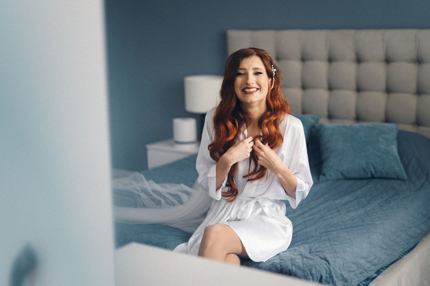 Joyful moment captured on bed wearing white silk robe against blue wall.