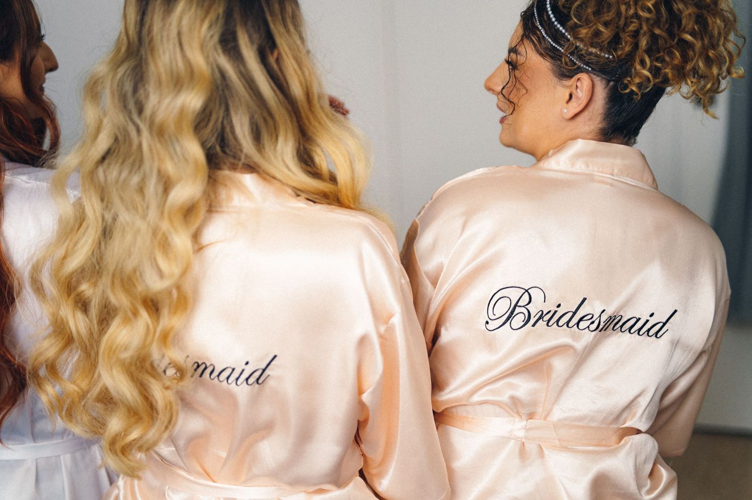 Detail shot of silk bridesmaid robes with embroidered text in rose gold color.