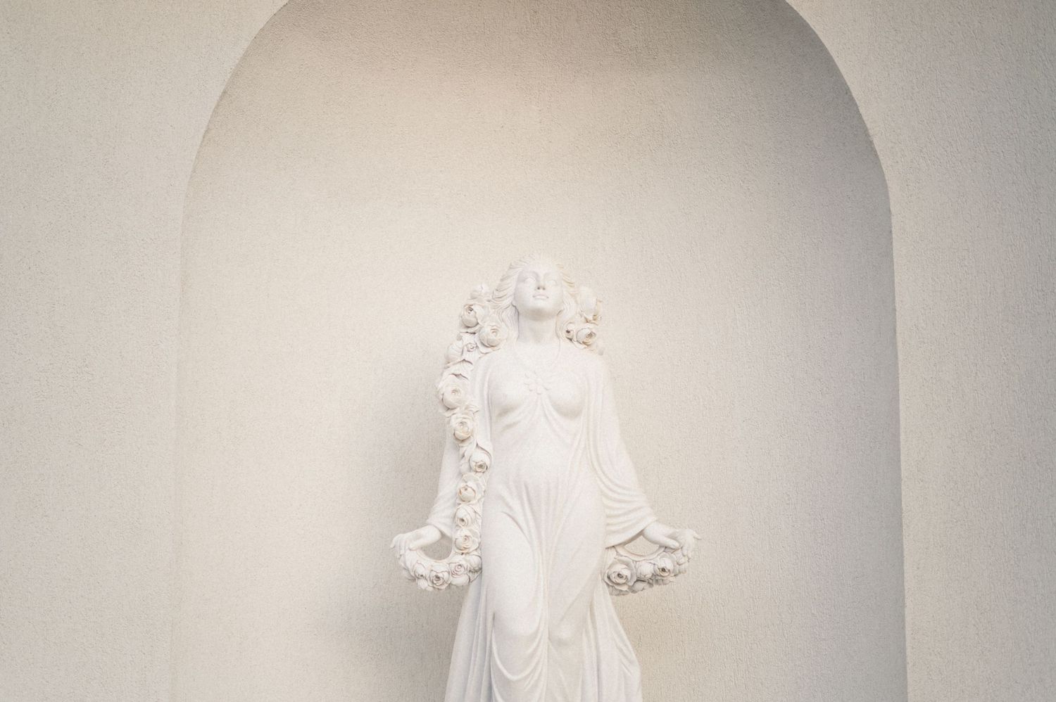 White wedding dress displayed in arched alcove against neutral wall.
