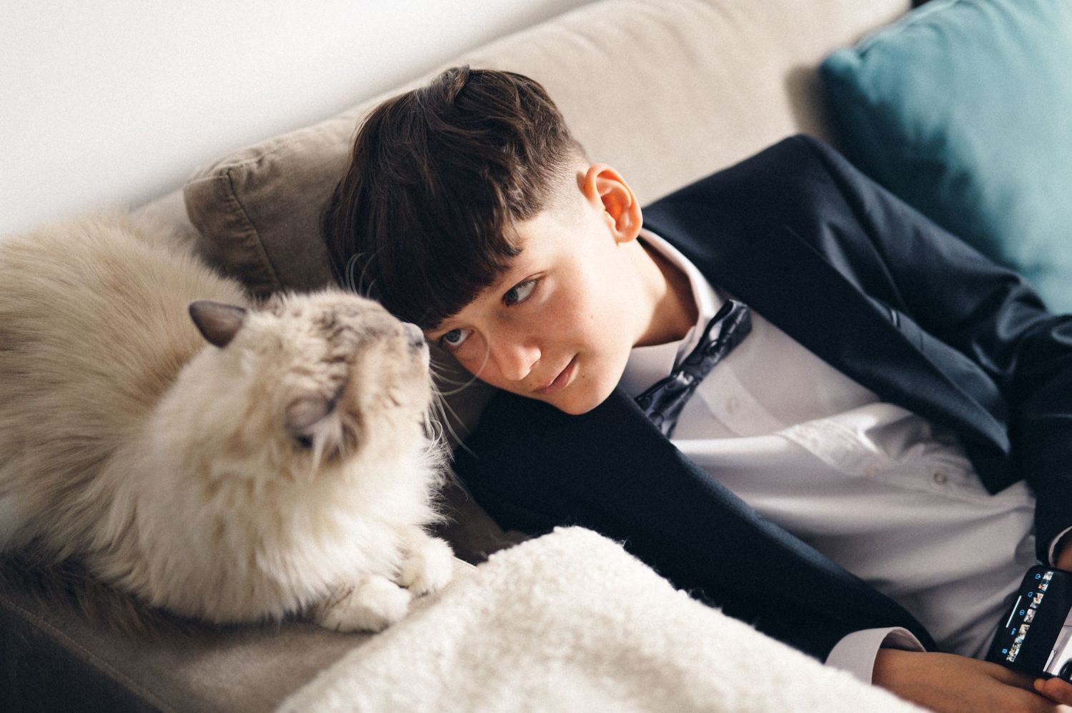 A young person in dark clothing relaxing on a couch with a fluffy white cat.