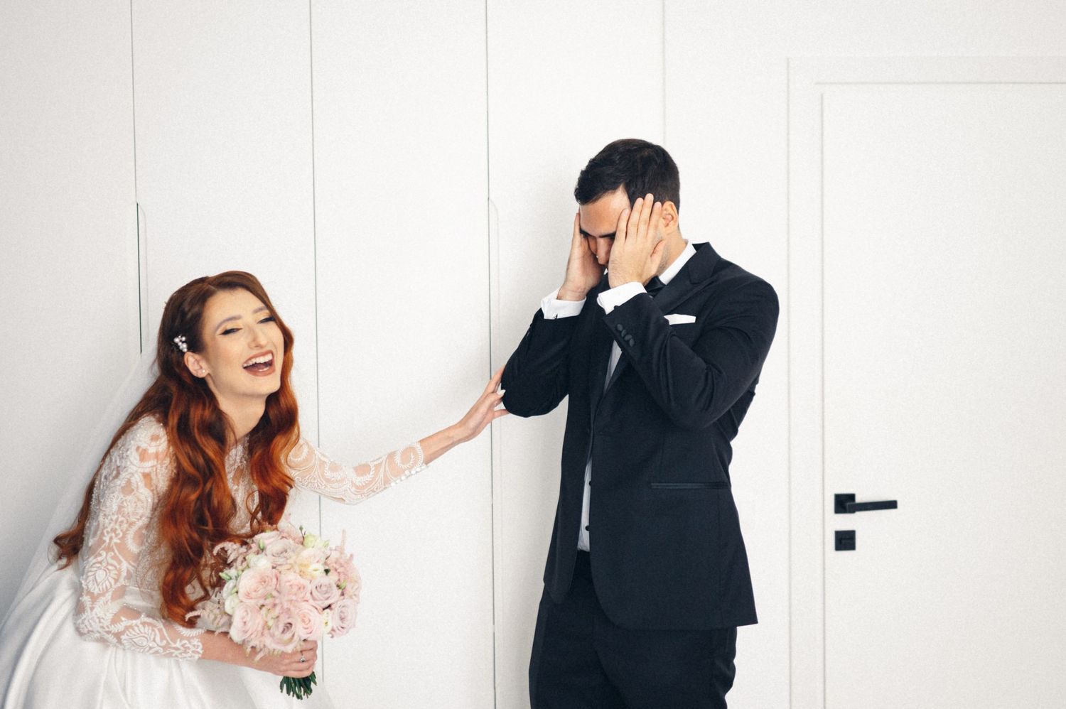 Wedding couple sharing emotional first look moment in white room.