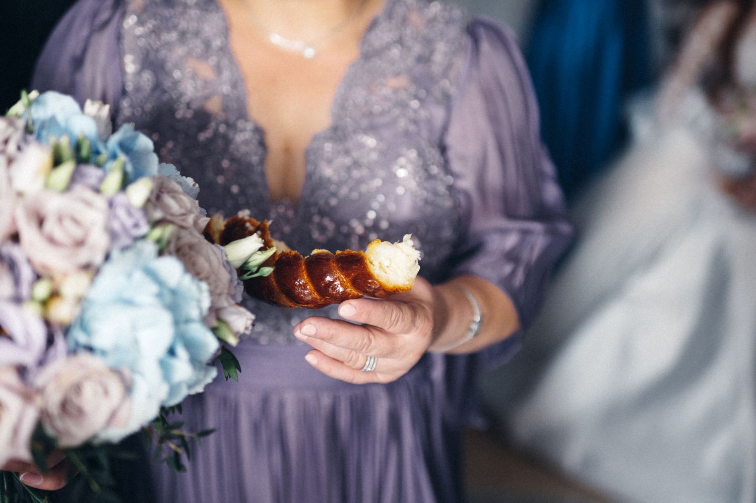 Close-up of bridesmaid holding purple bouquet and delicate details during wedding celebration.