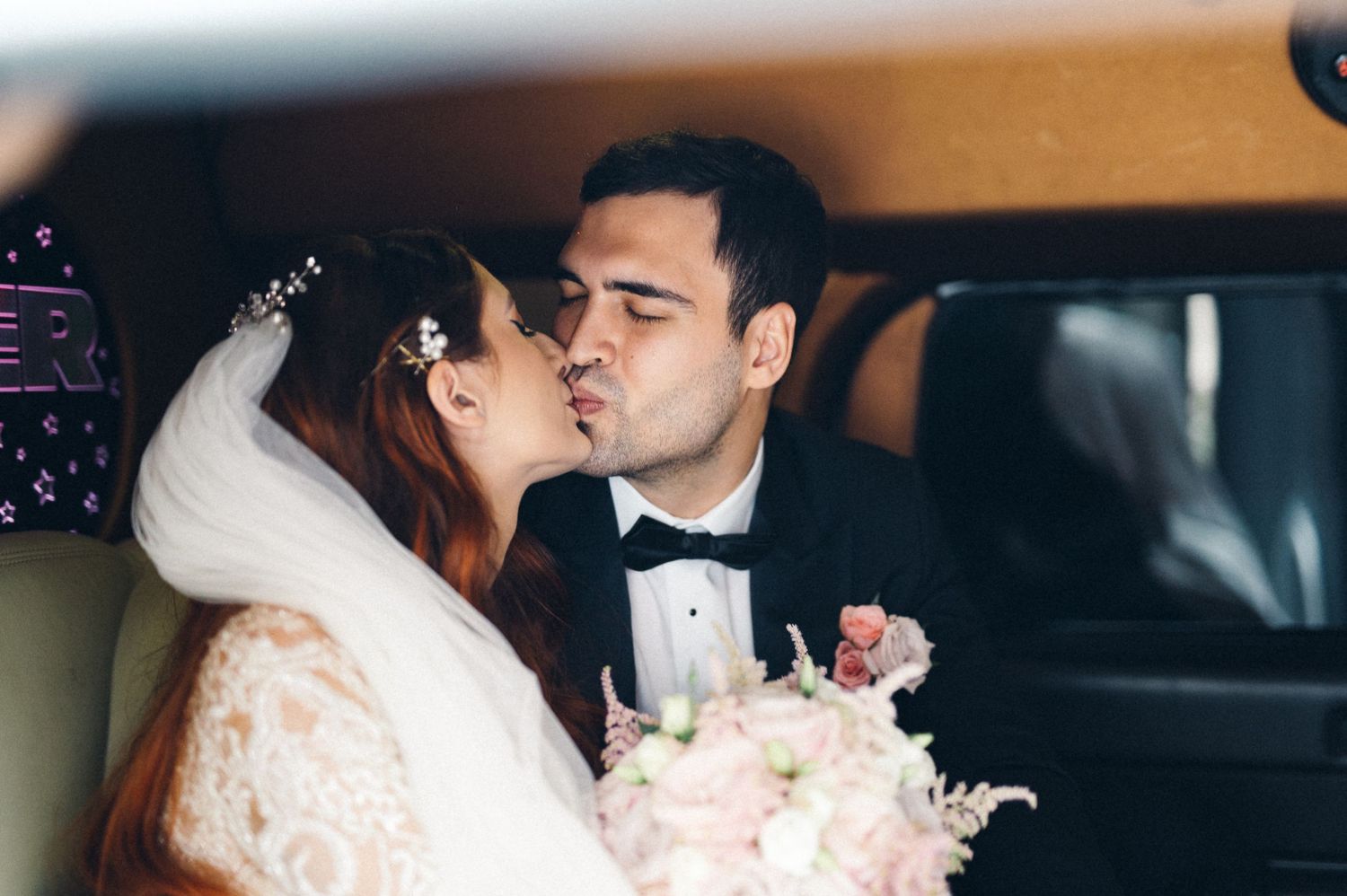 Romantic moment captured between newlyweds in wedding attire inside vehicle.