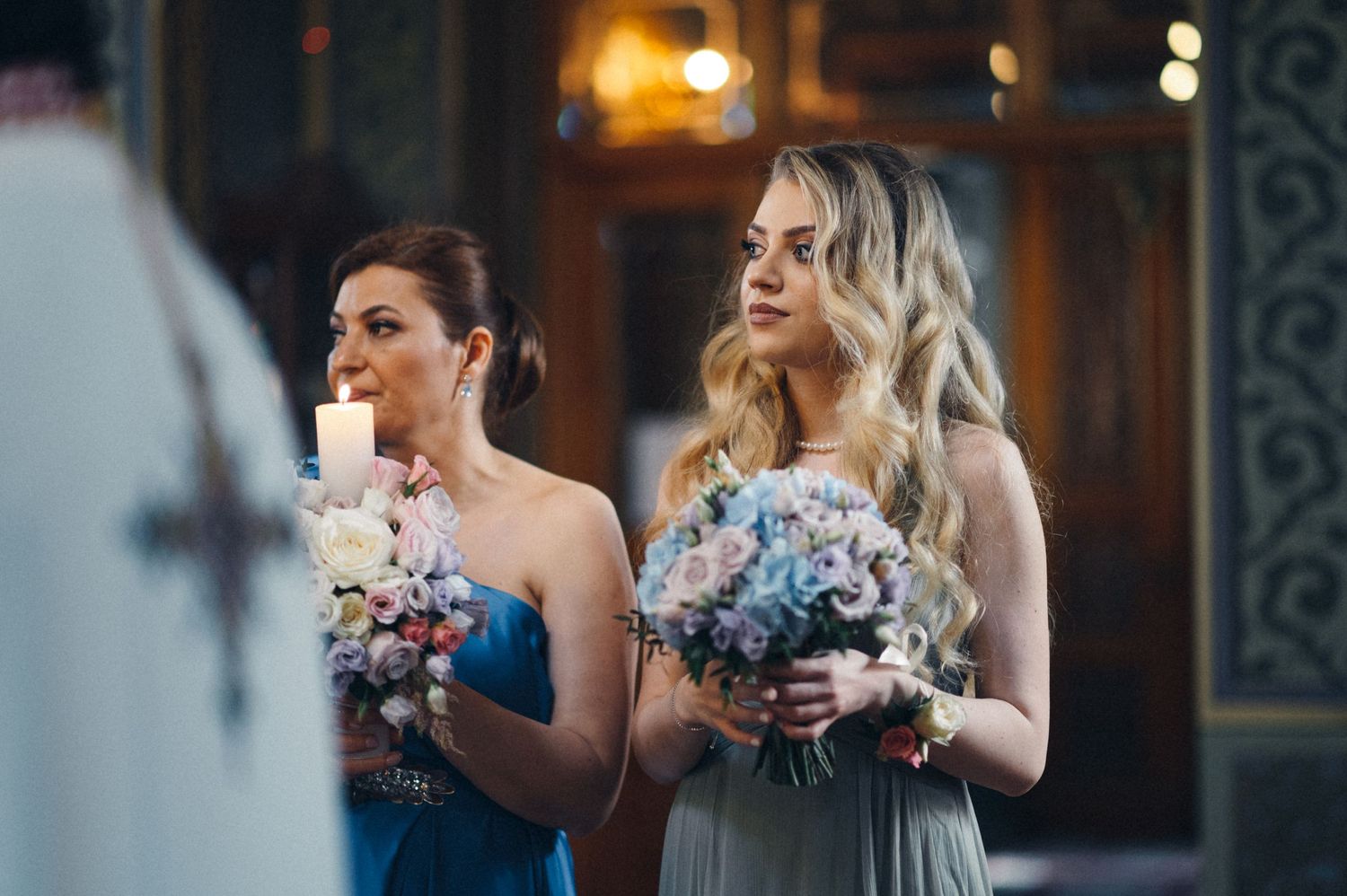 Bridesmaids in formal attire holding floral bouquets during church ceremony.