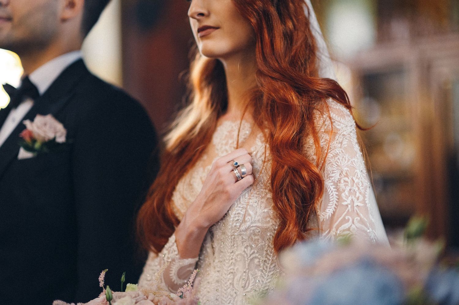 Close-up of bride in lace dress with flowing red hair during ceremony.