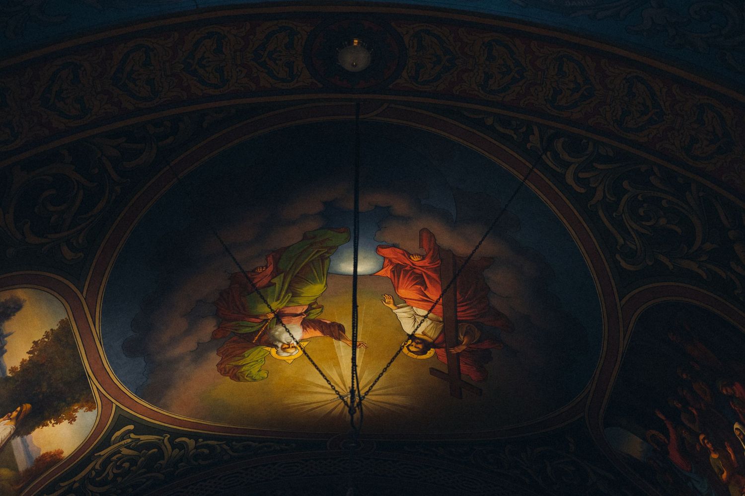 Ornate church ceiling with detailed artwork illuminated by warm lighting and dark edges.