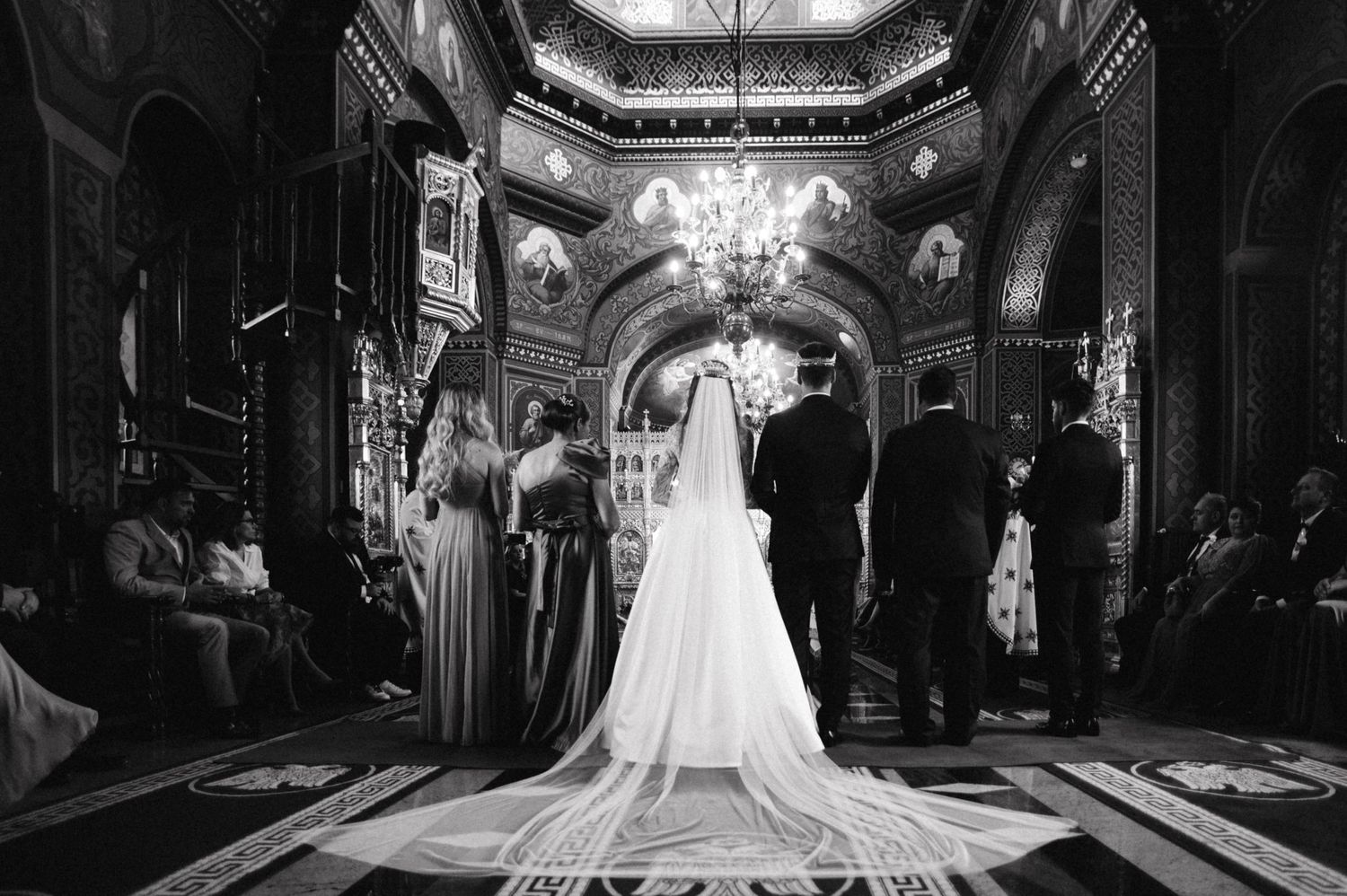 Black and white wide shot of wedding ceremony in ornate church with long aisle and high ceilings.