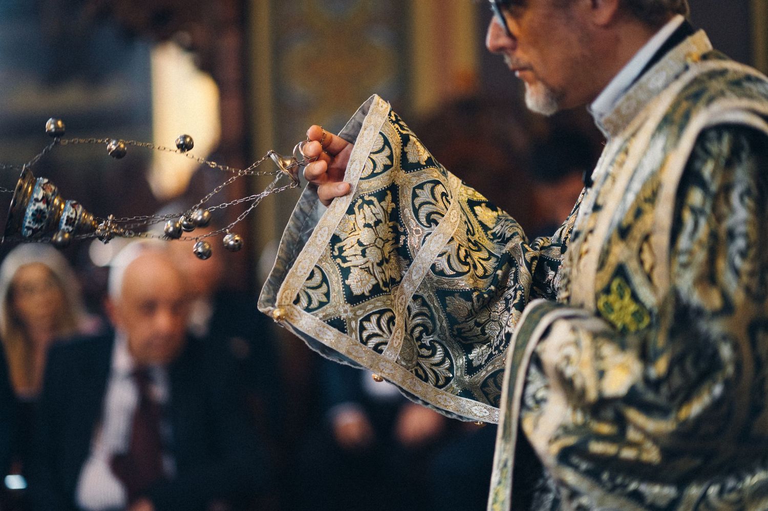 Close-up of priest holding ornate ceremonial censer during Orthodox church service.