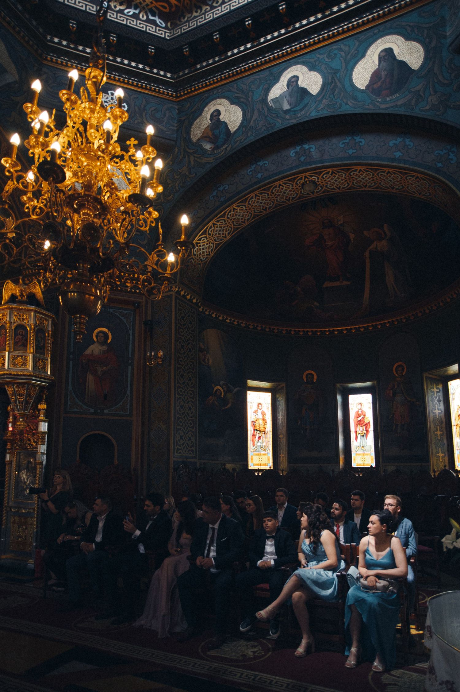 Ornate Orthodox church interior with golden chandelier and painted ceiling during ceremony.