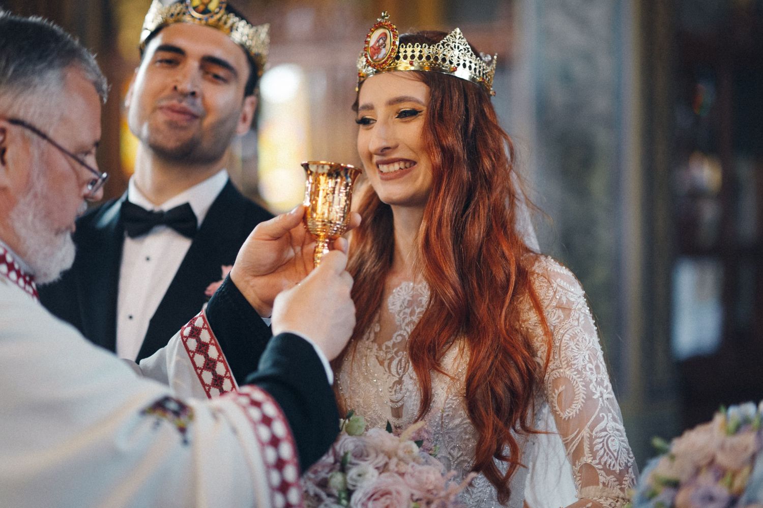 Intimate moment during Orthodox wedding ceremony with ornate gold crowns and white robes.