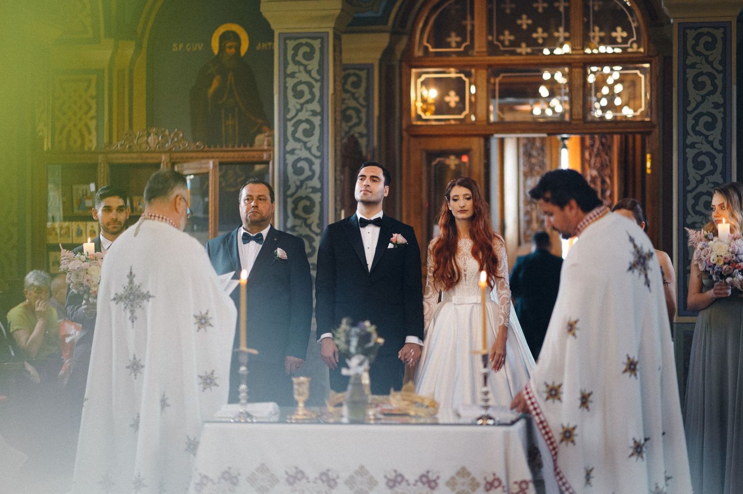 Orthodox wedding ceremony at ornate altar with priests in traditional white robes performing rituals.