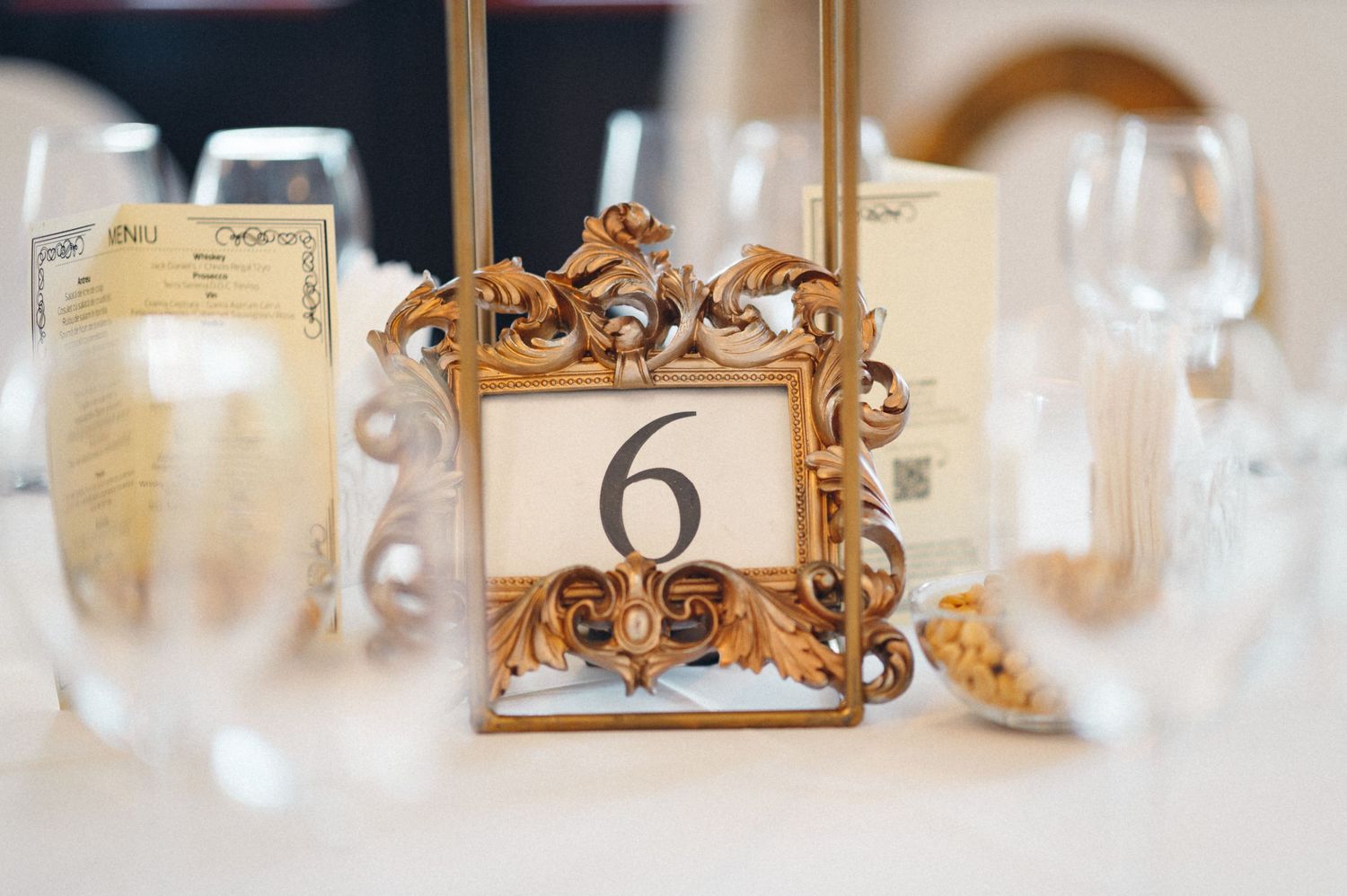 Ornate gold baroque frame displaying table number six between champagne glasses.