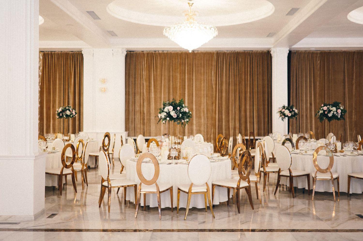 Modern wedding venue with gold-accented chairs, white linens, and elegant floral centerpieces.