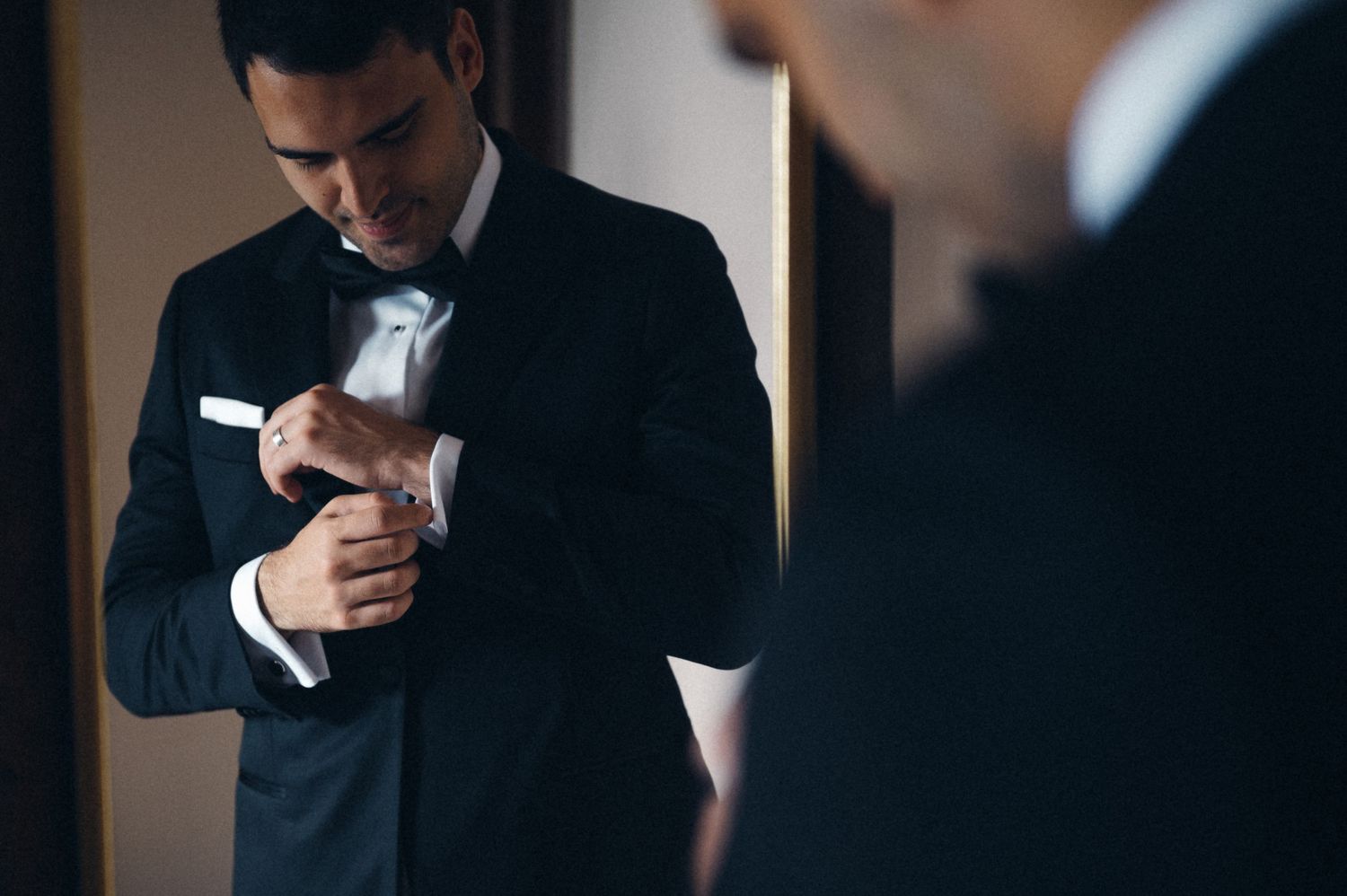 A close-up shot of formal attire preparation, adjusting white cuffs and suit jacket.