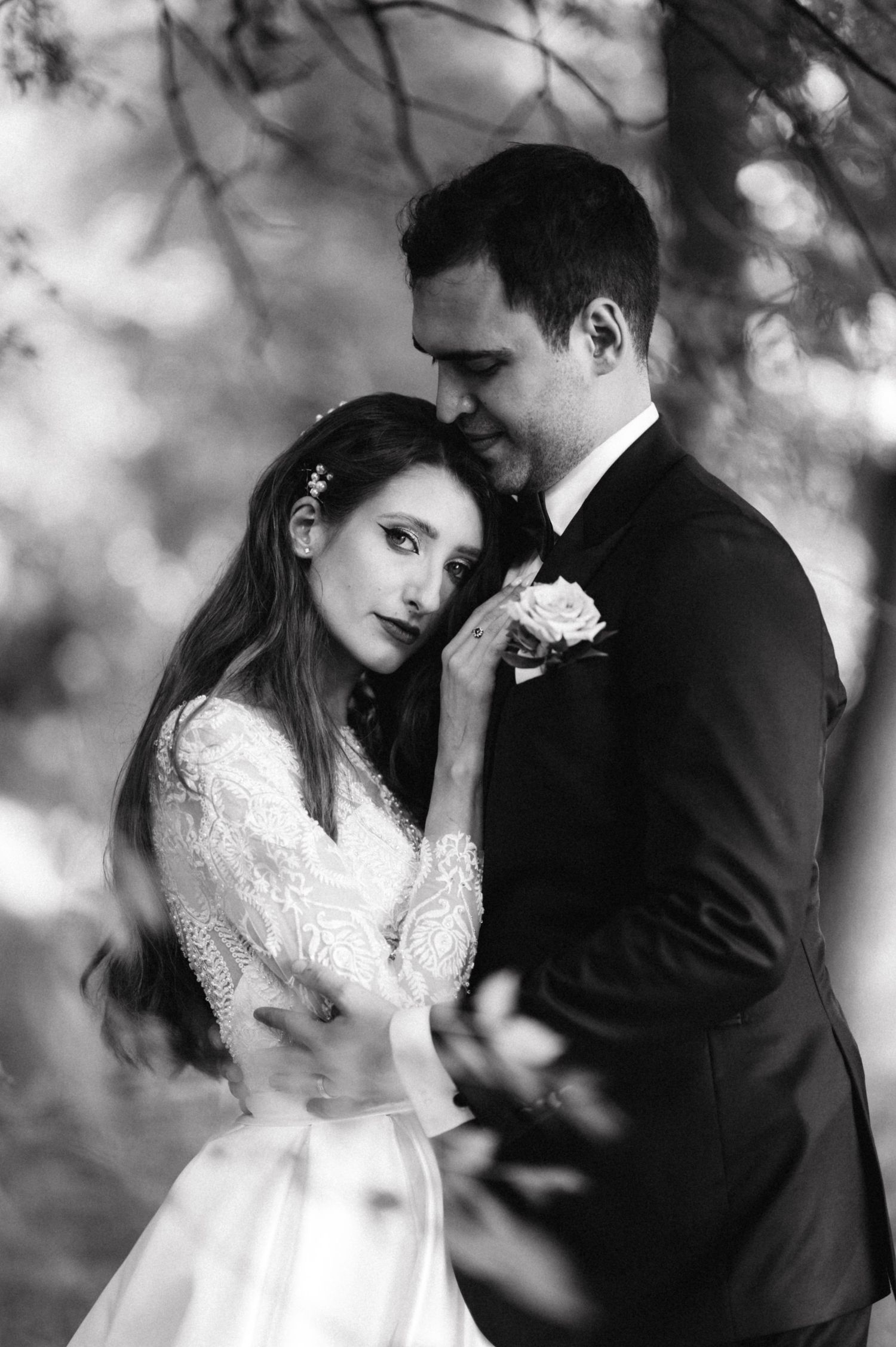 An intimate black and white wedding portrait showing a tender moment between newlyweds in a natural setting.