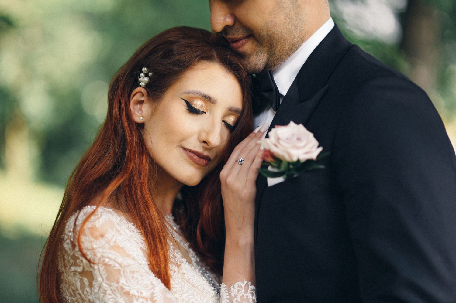 A close-up wedding photo capturing a tender moment between newlyweds with a pink rose boutonniere.