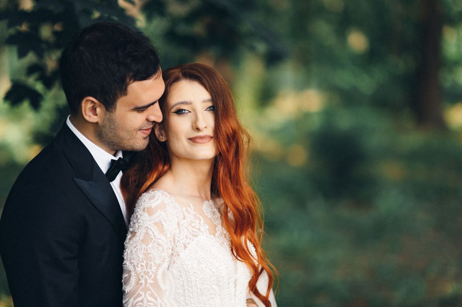 A tender outdoor wedding portrait capturing a sweet moment between the couple amid green foliage.