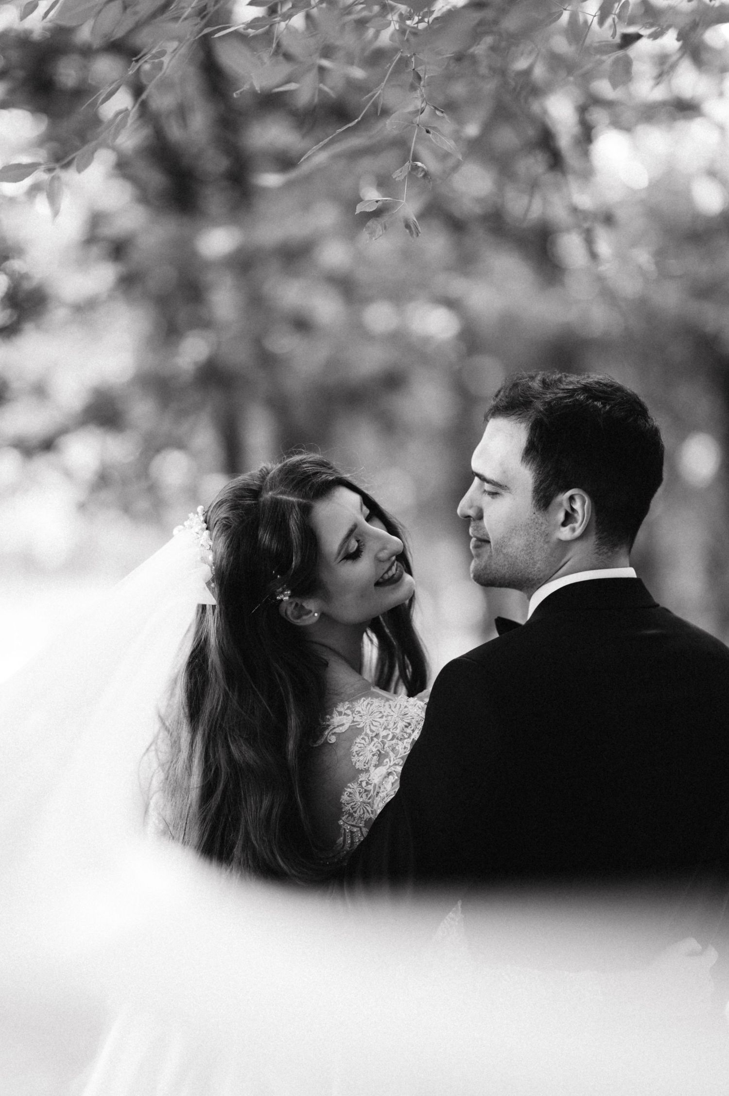 Black and white wedding portrait showing a romantic moment between newlyweds in a natural outdoor setting.