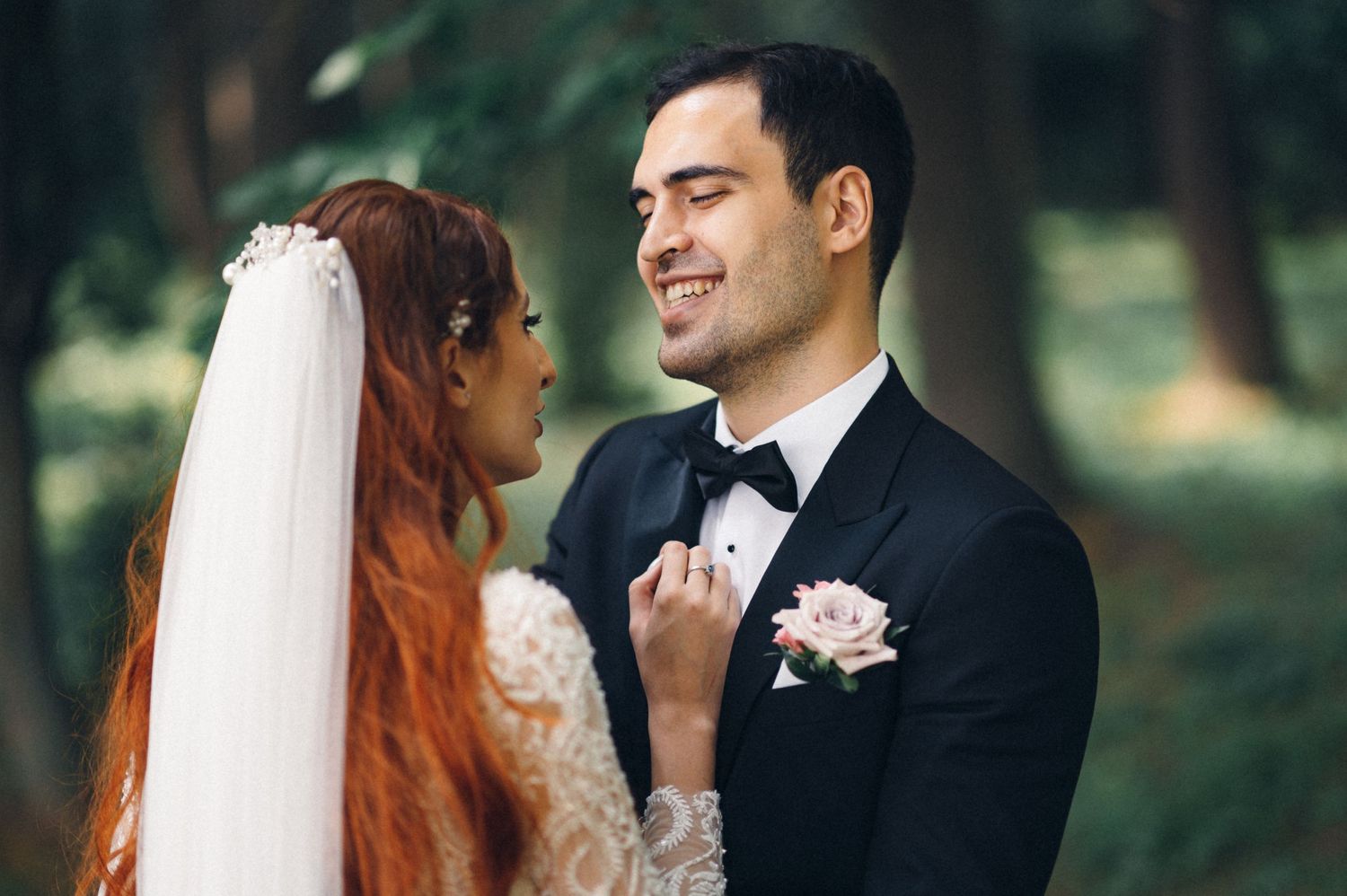 Wedding couple shares an intimate moment outdoors with bride wearing white lace dress and groom in black tuxedo.